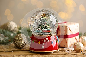 Beautiful snow globe with Christmas tree on wooden table against blurred festive lights