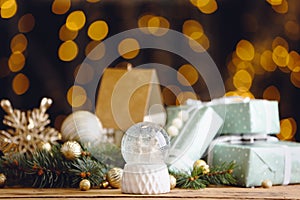 Beautiful snow globe, gifts and Christmas decor on wooden table against blurred festive lights
