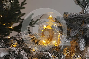 Beautiful snow globe with house model, glowing fairy lights inside and Christmas decor on wooden table