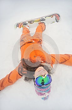 Beautiful snowboard girl lies on the snow looking at the camera.