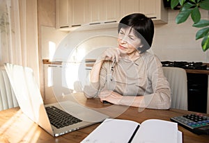 Beautiful sophisticated elderly woman holding glasses, talking on video communication on laptop.