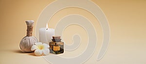 Beautiful spa composition with candle, frangipani flower, oil flask and herbal ball on beige background.
