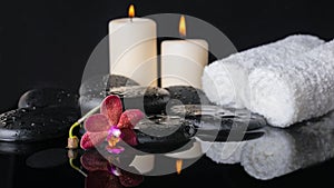 Beautiful spa concept of zen stones with drops, purple orchid (phalaenopsis), candles with reflection on water, white towels
