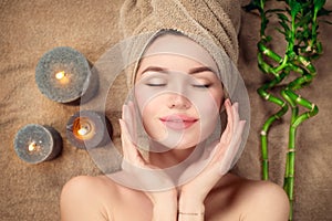 Beautiful spa woman with a towel on her head lying and touching face skin. Skincare