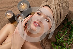 Beautiful spa woman with a towel on her head lying and touching face skin. Skincare. Beauty smiling model girl in spa salon