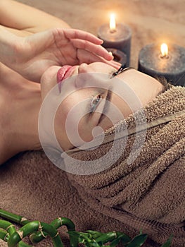 Beautiful spa woman with a towel on her head lying and touching face skin. Skincare. Beauty smiling model girl in spa salon