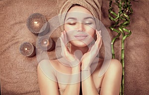 Beautiful spa woman with a towel on her head lying and touching face skin. Beauty smiling model girl in spa salon