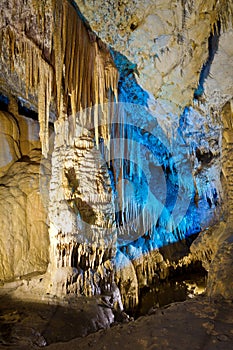 Beautiful speleothem stalagnata, stalactites, stalagmites in natural cave illuminated by color lights