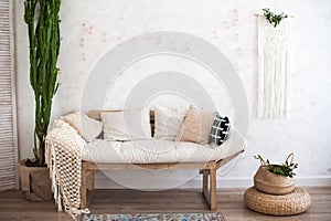 Beautiful sping decorated interior in white textured colors. Living room, beige sofa with a rug and a large cactus.