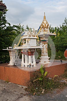 A beautiful spiritual house with dragons, figurines and incense bowls is standing in front of a residential building in Thailand