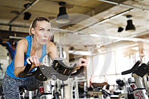Beautiful sport woman cycling on stationary bike in gym. Routine workout for woman& x27;s physical and mental health.