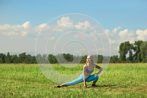 Beautiful sport woman doing stretching fitness exercise in city park at green grass.