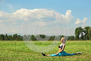 Beautiful sport woman doing stretching fitness exercise in city park at green grass.