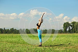 Beautiful sport woman doing stretching fitness exercise in city park at green grass.