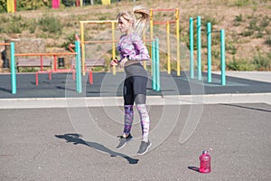 Beautiful and sportive blonde girl doing jumps on the street sports ground.