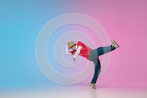 Boy dancing hip-hop in stylish clothes on gradient background at dance hall in neon light.