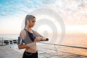 Beautiful sportive girl looking at watch during sunrise over seaside.