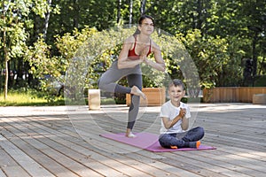 Beautiful sportive mom and little son do yoga in the morning park together