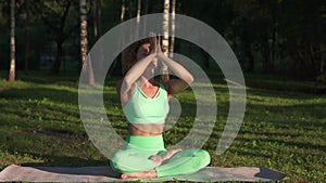 Beautiful sportive woman with closed eyes meditates in siddhasana position on the grass in the morning of a sunny day