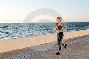 Beautiful sportive woman in headphones running at the seaside