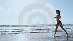 Beautiful sportive woman running along beautiful sandy beach, healthy lifestyle, enjoying active summer vacation near