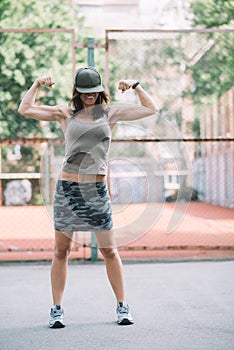 Beautiful sports girl in khaki clothes and a cap on the playground shows biceps and smiles. Healthy lifestyle.