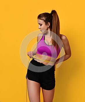 Beautiful sports woman measure her waist with tape measure on yellow background weight loss concept