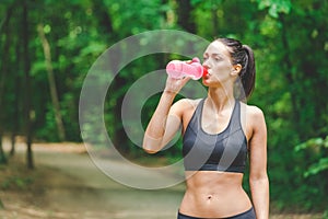 Beautiful sportswoman runner drinking water from bottle next to running track outdoors.