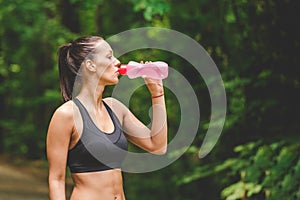 Beautiful sportswoman runner drinking water from bottle next to running track outdoors.