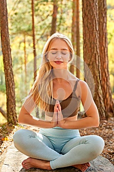 Beautiful sporty blonde woman sit meditating in the forest photo