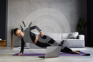 Beautiful sporty cheerful woman is doing side plank exercise watching video on the internet and repeating the tasks