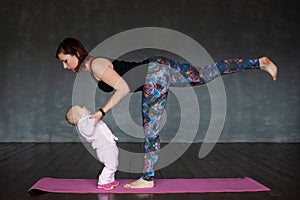 Beautiful sporty fit woman practices yoga asana Virabhadrasana holding her baby.