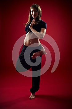 Beautiful sporty fit yogi woman practices yoga asana Vrikshasana - Tree pose on the red background. studio shot