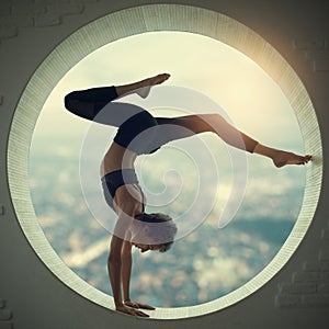 Beautiful sporty fit yogi woman practices yoga handstand asana Bhuja Vrischikasana - Scorpion handstand pose in a window