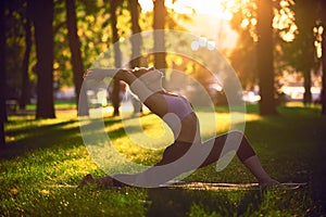 Beautiful young woman practices yoga asana Virabhadrasana 1 - warrior pose 1 in the park at sunset