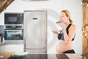 Beautiful sporty fit young pregnant woman having a healthy snack in home kitchen. Healty lifestyle concept.