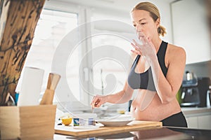 Beautiful sporty fit young pregnant woman preparing healthy meal in home kitchen. Healty lifestyle concept.