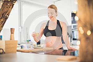 Beautiful sporty fit young pregnant woman preparing healthy meal in home kitchen. Healty lifestyle concept.
