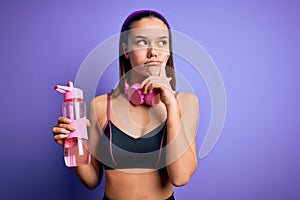 Beautiful sporty girl doing sport using headphones drinking bottle of water to refreshment serious face thinking about question,