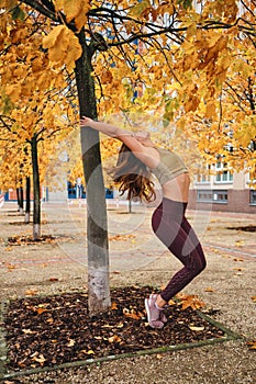 Beautiful sporty girl in sportswear practicing yoga under tree on street
