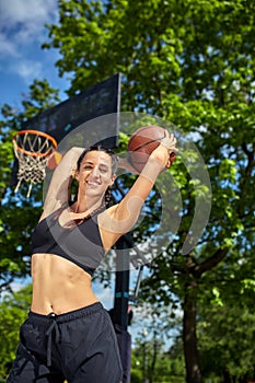 Beautiful, sporty latin girl with a basketball under the ring on a street basketball court. Sport motivation, healthy
