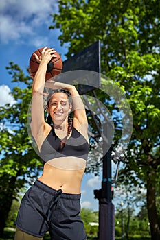 Beautiful, sporty latin girl with a basketball under the ring on a street basketball court. Sport motivation, healthy