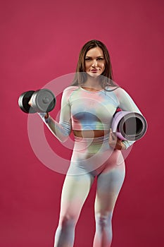 Beautiful sporty woman with dumbbell in pink studio.