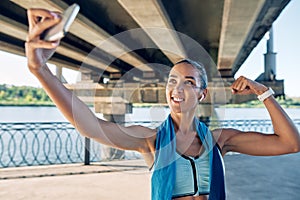 Beautiful sporty woman making selfie flexing her muscles