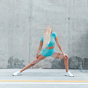 Beautiful sporty young woman fitness model with blonde hair in fashion blue sportswear with white sneakers start stretching