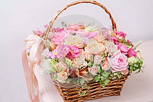 Flowers arrangement with various of colors in wicker basket on pink table. beautiful spring bouquet. bright room, white