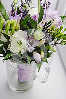 Beautiful spring bouquet of wedding flowers buttercup ranunculus, fresia, lavender in vase with violet tape. Pastel