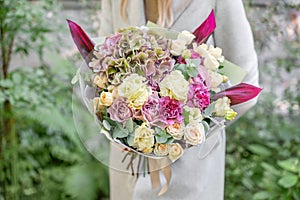 Beautiful spring bouquet. Young girl holding a flowers arrangement with various of colors. In the Park, blurred leaves