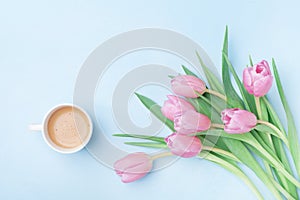 Beautiful spring breakfast on Mothers or Womans day. Bouquet of pink tulips and coffee cup on blue pastel table top view. Flat lay