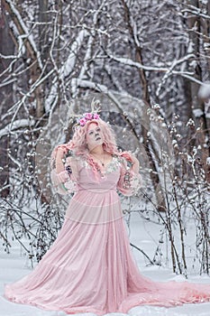 A beautiful spring fairy, a dryad with deer antlers and a crown and a light pink dress in a snowy forest.A fabulous photo. The